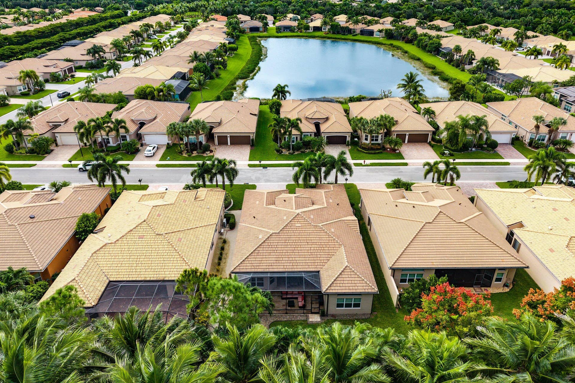 Aerial perspective of a residential community featuring tile roofs, paved roadways, palm tree landscaping, and a central water feature