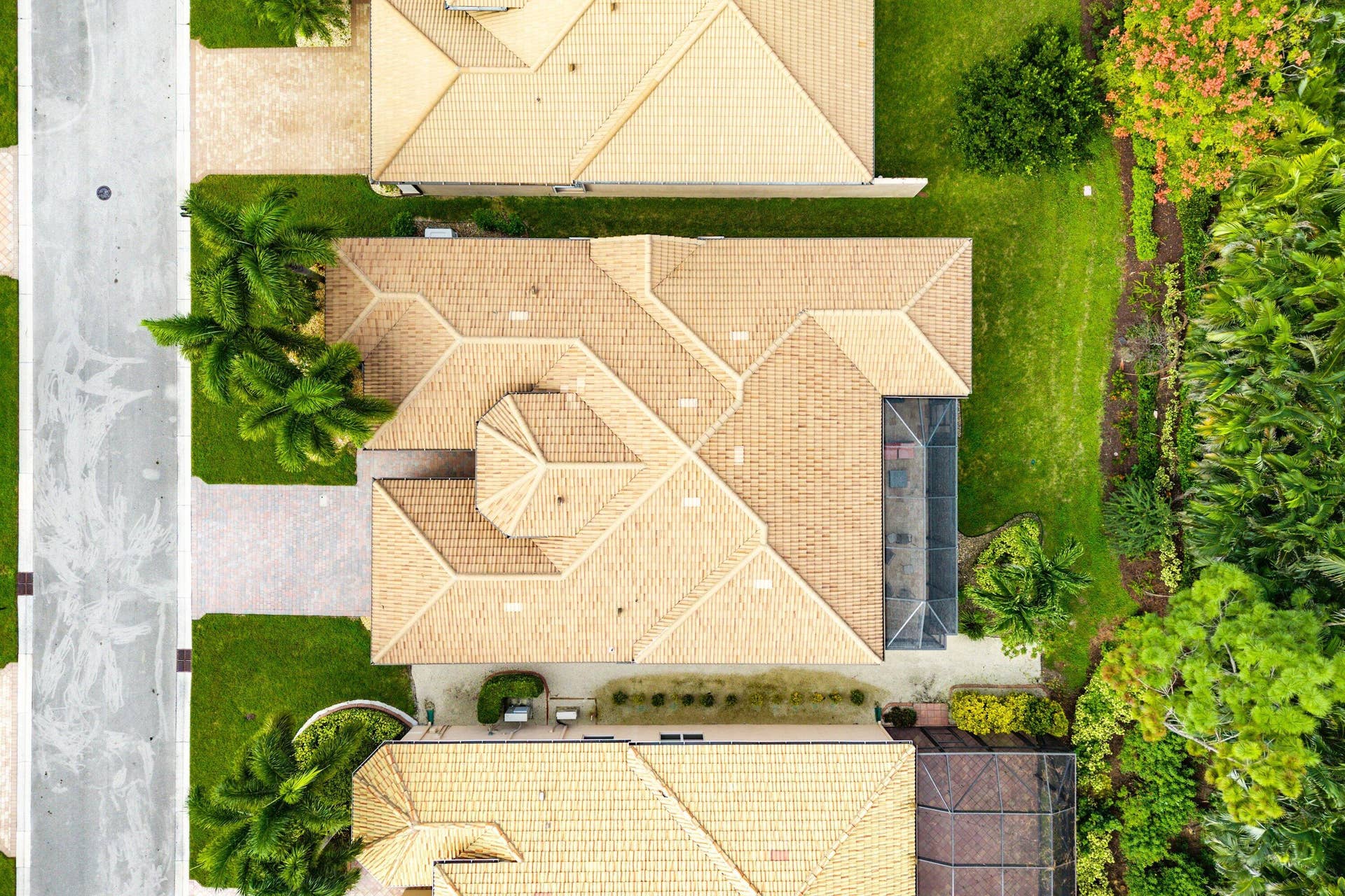 Aerial view featuring a multi-gabled tile roof, a screened-in enclosure, concrete driveway, and landscaped perimeter