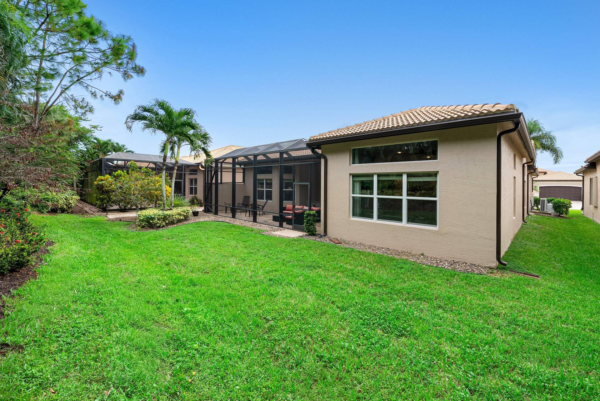 Stucco exterior featuring a screened-in lanai, multi-pane windows, a tiled roof, and a manicured lawn