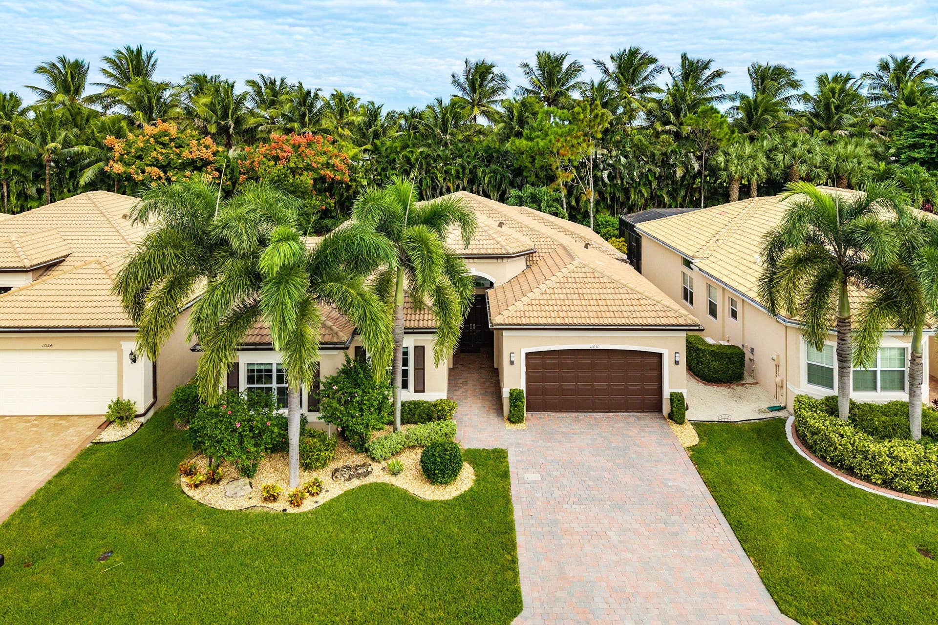 Stucco exterior featuring a multi-hipped tile roof, paver driveway, attached two-car garage, and mature palm tree landscaping