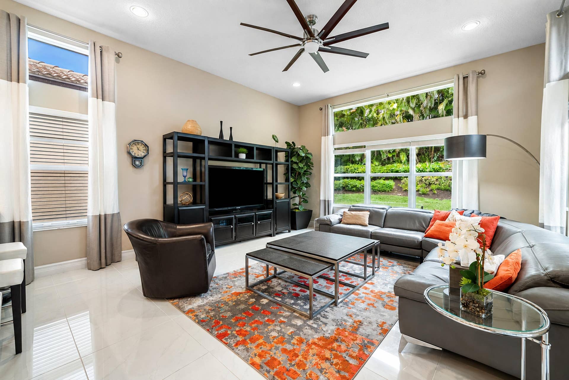 High-ceiling living area featuring large windows, neutral-toned tile flooring, recessed lighting, and a multi-blade ceiling fan