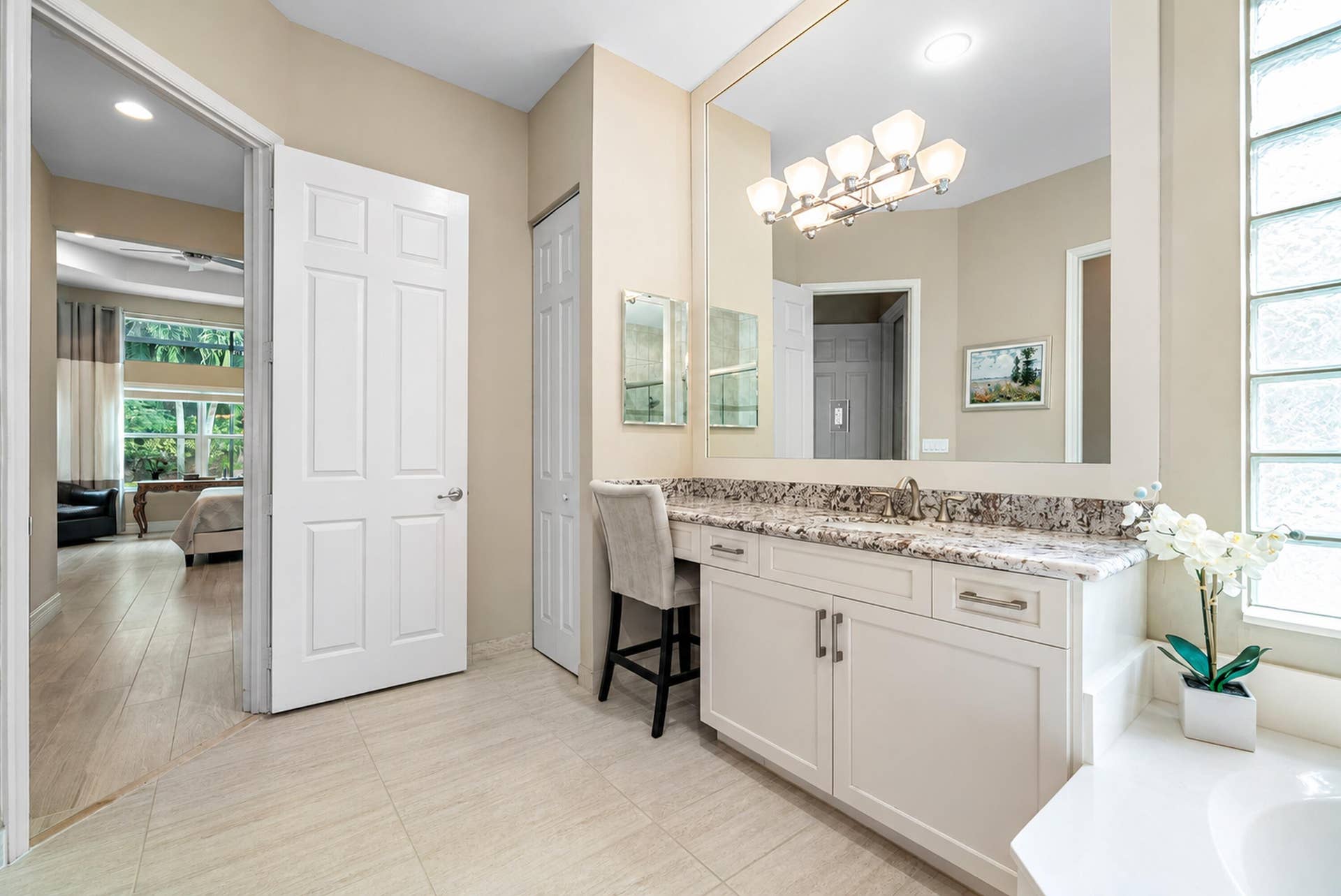 Bathroom vanity featuring white cabinetry, stone-surface countertop with an integrated sink, full-width wall mirror, multi-bulb light fixture, and translucent glass block window