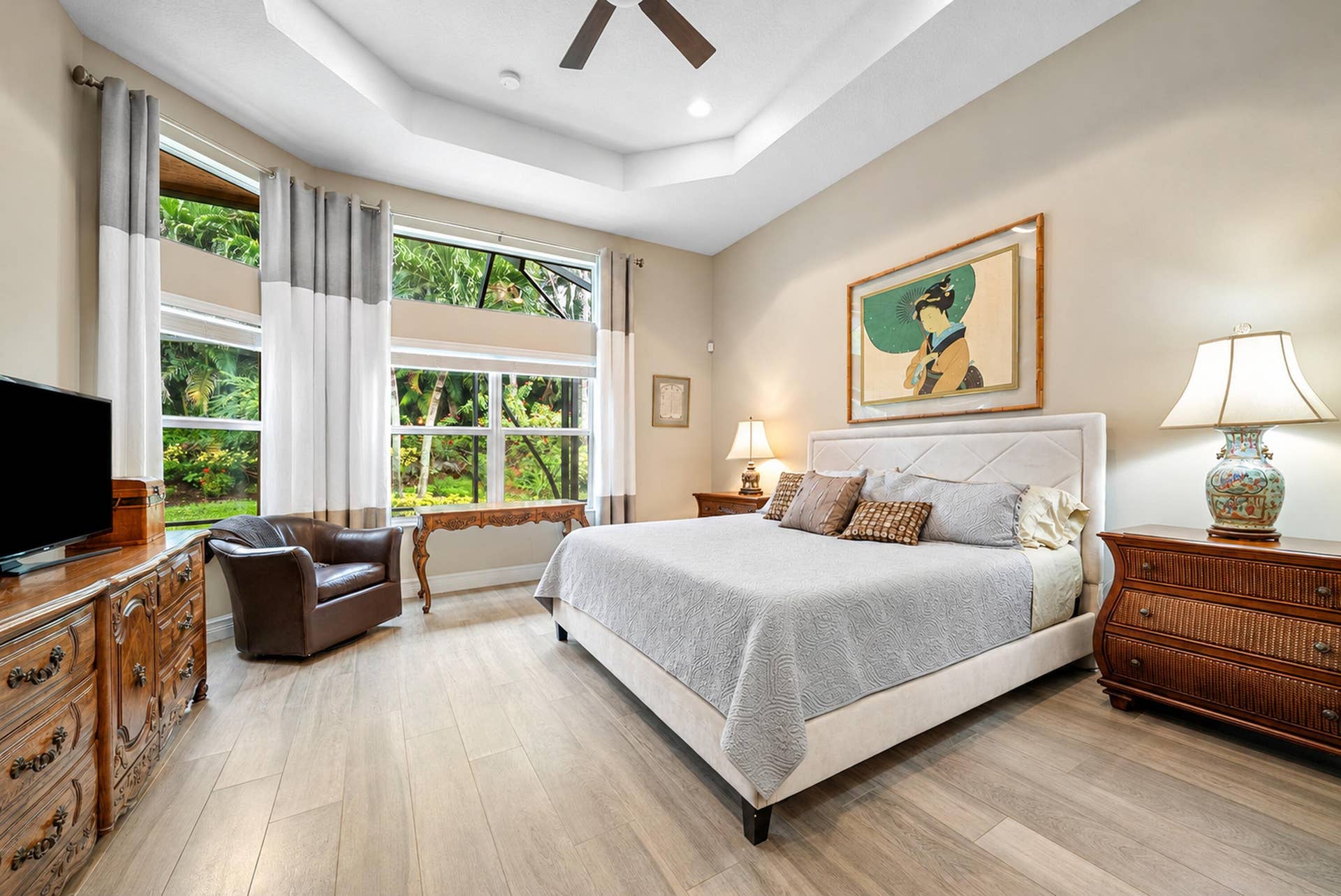 Tray ceiling with a central fan, light-toned wood-finish flooring, and multiple tiers of windows