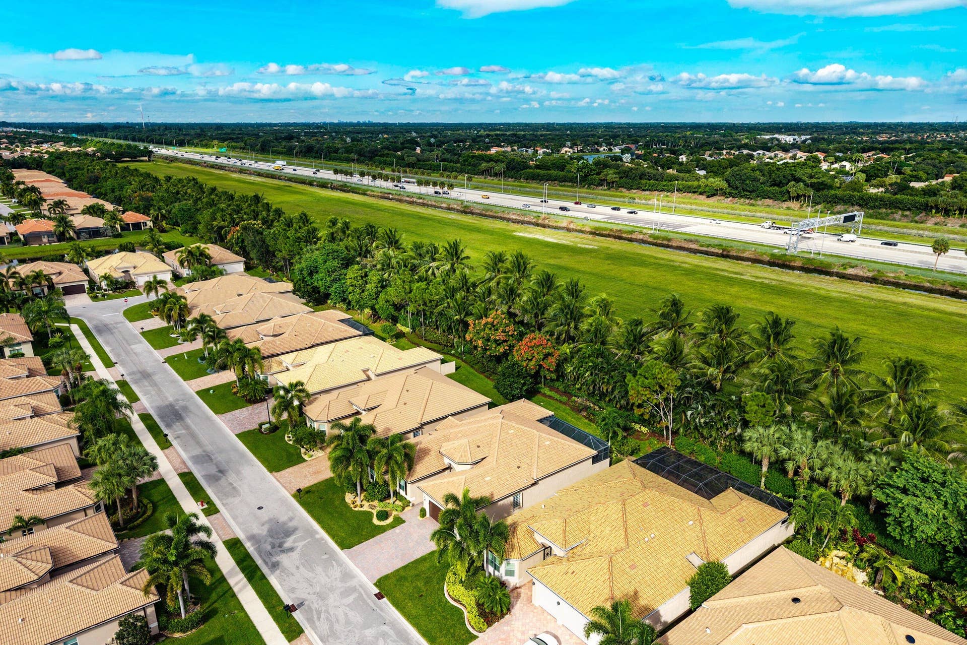 Aerial perspective of a suburban neighborhood featuring tile-roofed residences, paved roadways, manicured lawns, and mature palm landscaping