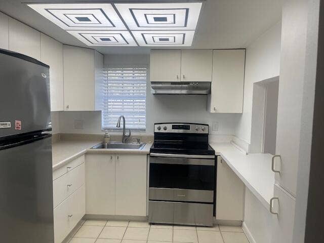 Kitchen featuring white cabinetry, stainless steel appliances, neutral solid-surface countertops, dual-basin sink with arched faucet, and recessed geometric-patterned ceiling lighting