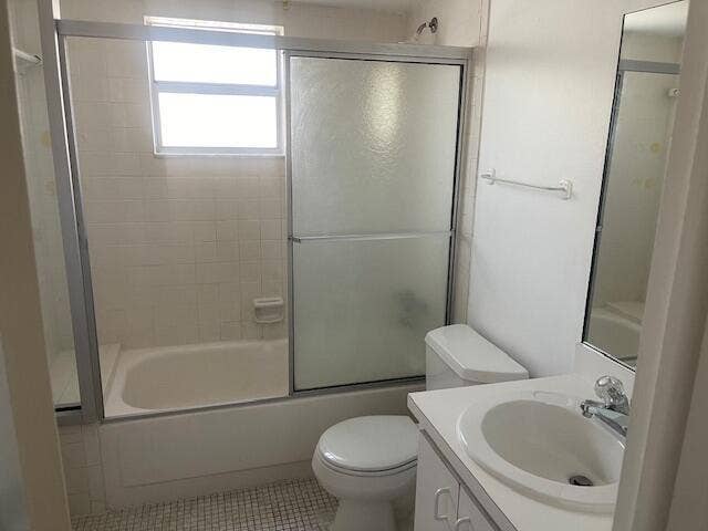 Bathroom featuring a combination bathtub and shower with a sliding glass enclosure, tile wall surround, single-basin vanity with a solid-surface countertop, and a wall-mounted mirror