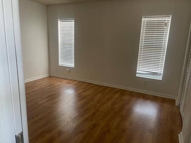 Interior space featuring wood-finish flooring, neutral wall tones, and two windows with horizontal blinds