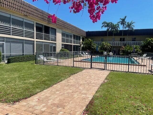 Common area featuring a paved walkway, swimming pool with metal fencing, manicured lawn, and mature palm trees