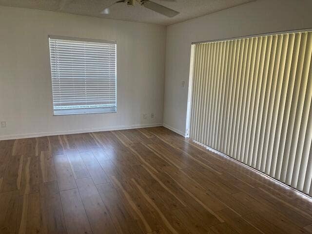 Interior space featuring wood-finish flooring, white walls, a ceiling fan, a standard window with horizontal blinds, and sliding glass doors with vertical blinds