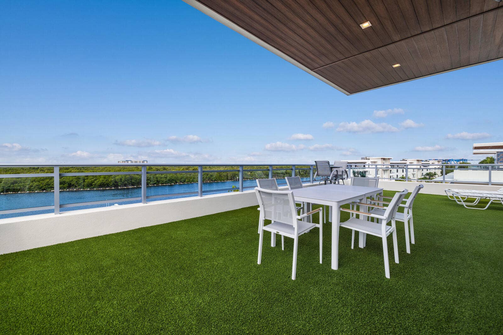 Expansive outdoor terrace featuring synthetic turf, metal railing, recessed lighting, and a wood-finish ceiling panel