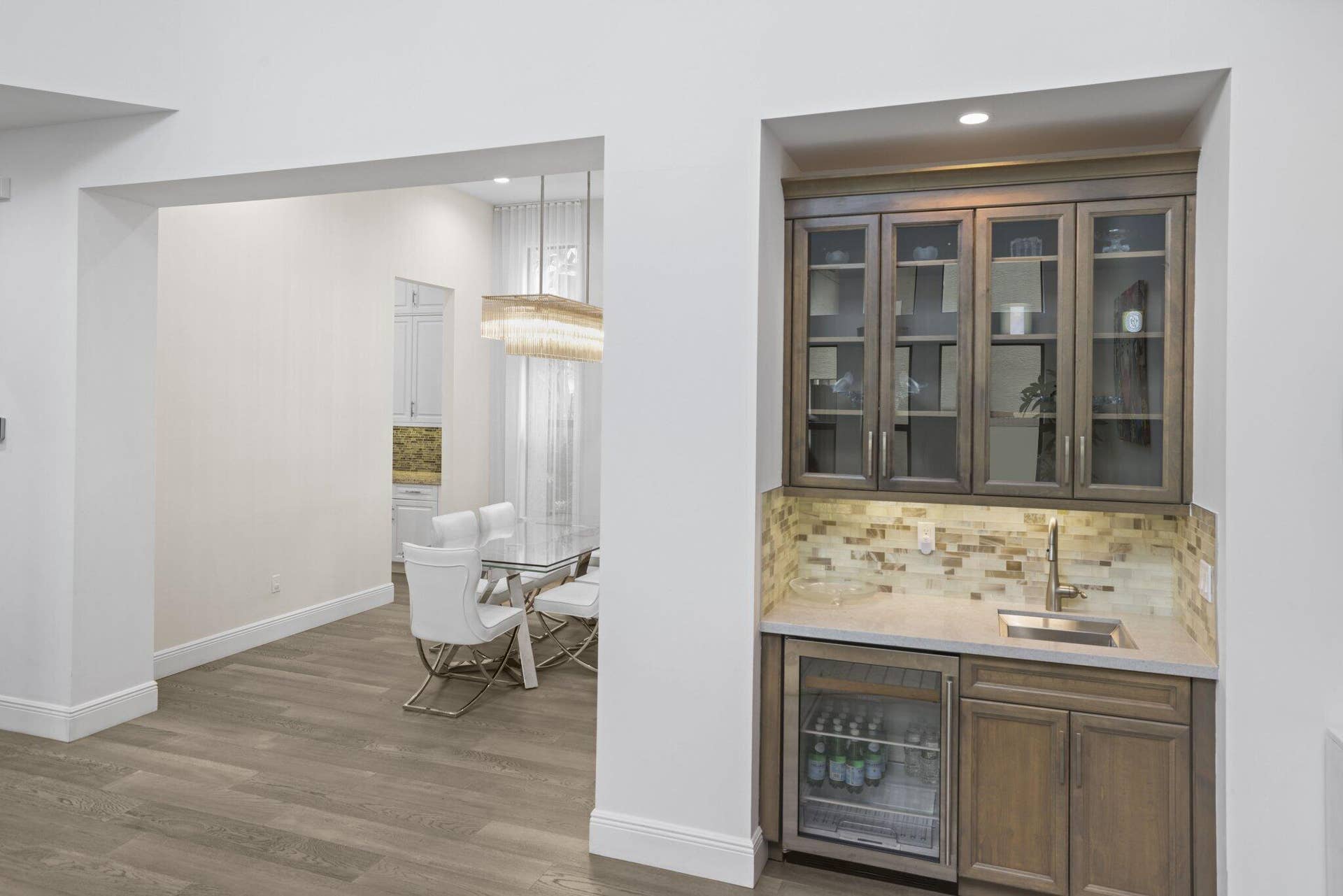 Built-in wet bar with glass-front cabinetry, under-cabinet lighting, and beverage refrigerator