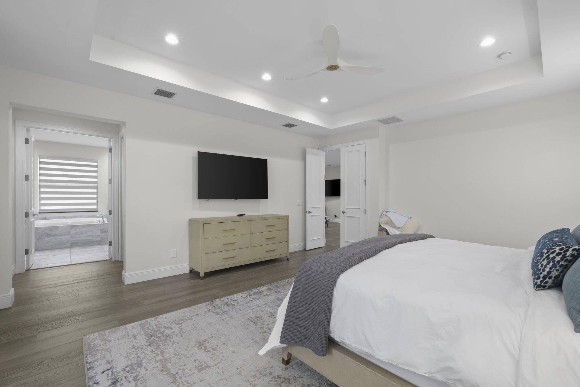 Tray ceiling with recessed lighting and a ceiling fan, wood-finish flooring, and a wall-mounted television