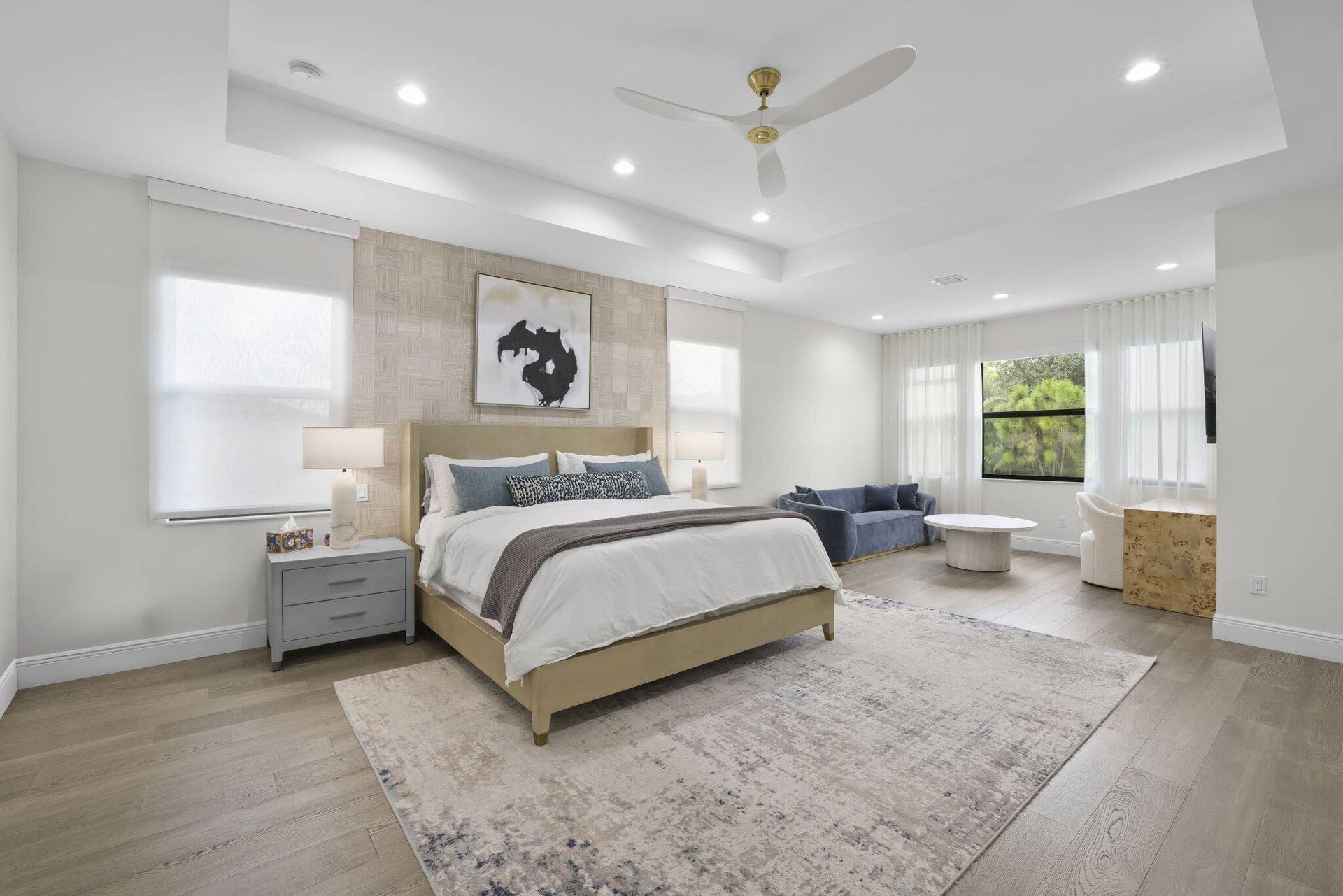 Tray ceiling with recessed lighting, wood-finish flooring, accent wall, ceiling fan, and large windows with roller shades
