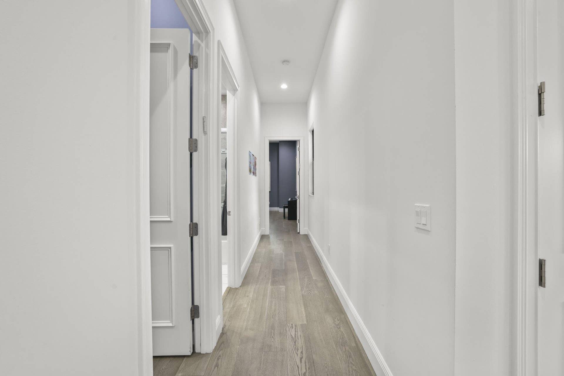 Recessed lighting illuminating a hallway with wood-finish flooring and multiple paneled doors
