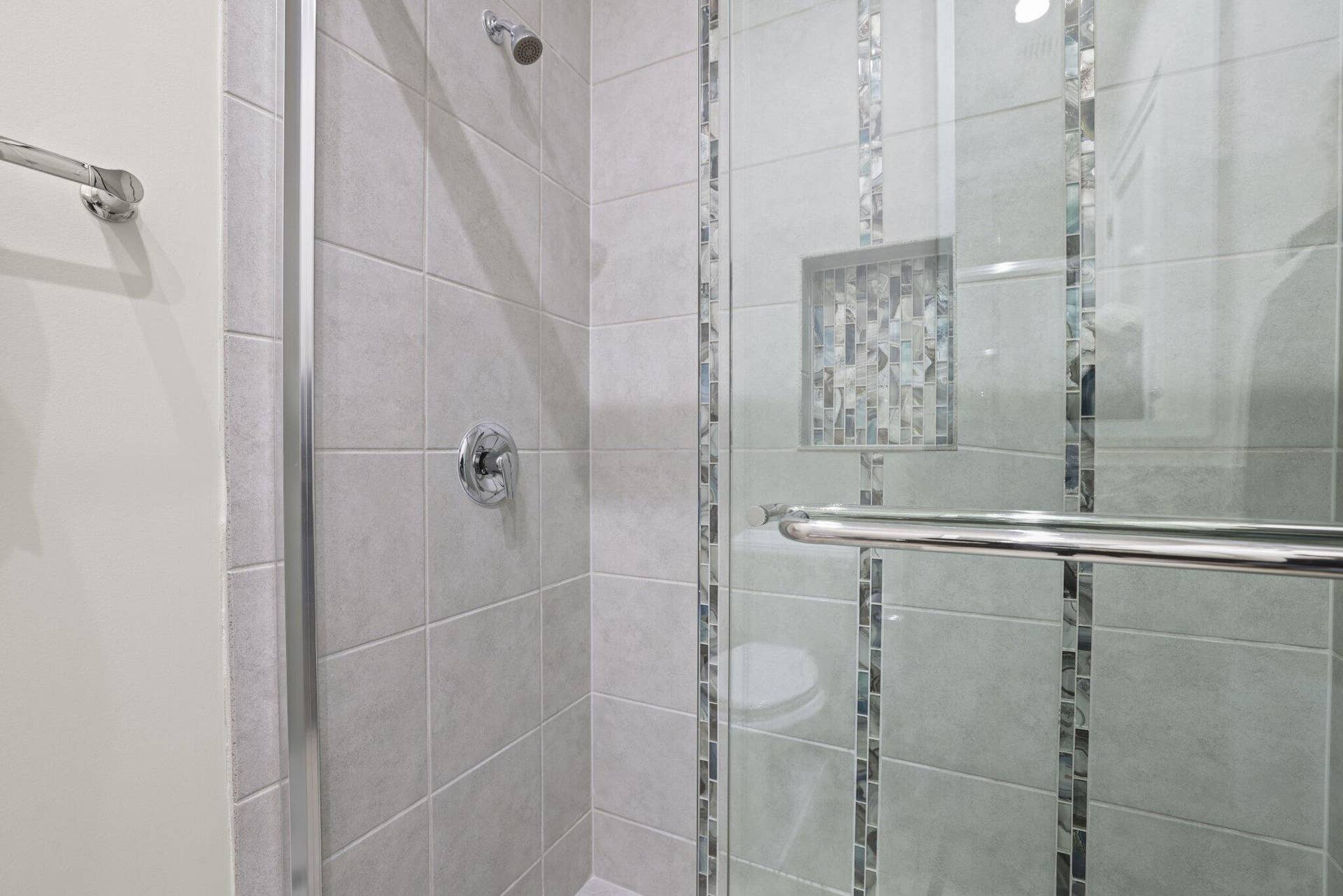 Tiled shower with glass enclosure, chrome fixtures, decorative mosaic tile accents, and a recessed niche
