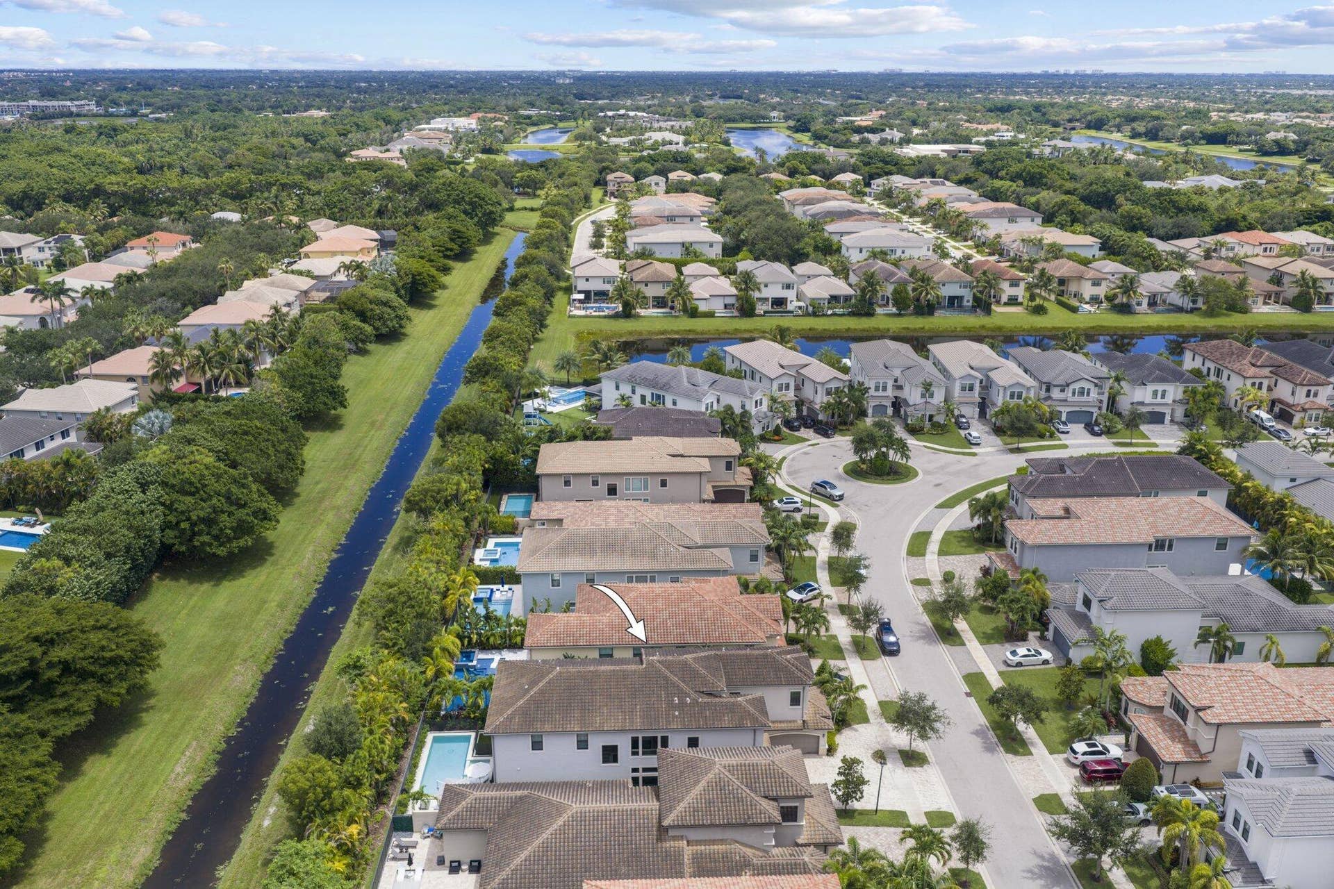 Aerial overview of a residential area with a prominent canal, several homes featuring private pools, and mature landscaping