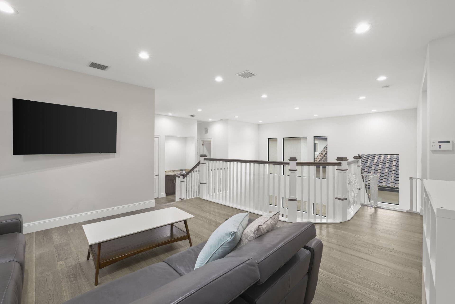 Open concept living area featuring wood-finish flooring, recessed lighting, and a white balustrade staircase with dark wood handrails