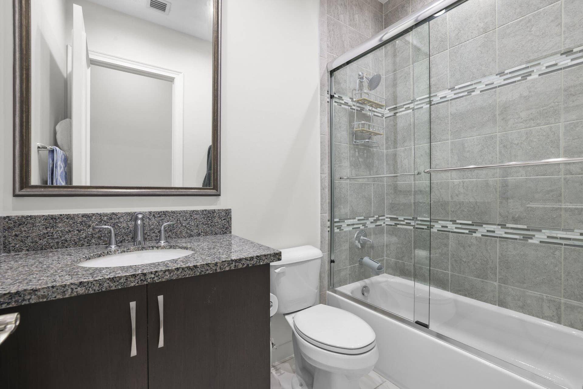 Built-in vanity with a stone countertop and undermount sink, framed mirror, full bathtub, and tiled shower surround with glass sliding doors