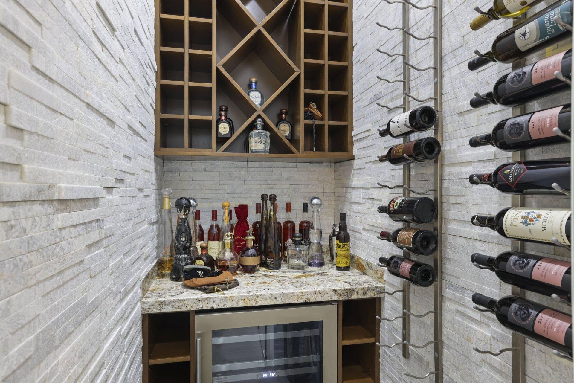 Stacked stone accent walls with built-in wine storage, wood-finish shelving, granite-style countertop, and integrated beverage cooler