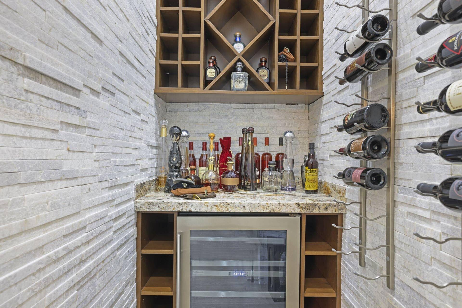 Stone-clad walls framing a built-in bar area with a wood-finish wine rack, stainless steel beverage refrigerator, and a stone countertop