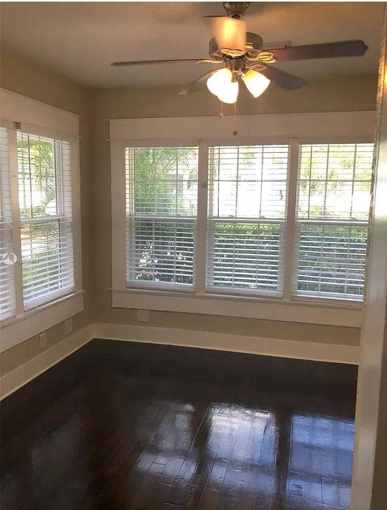 Multi-pane windows with horizontal blinds, dark wood-finish flooring, and a ceiling fan with integrated multi-globe light fixture