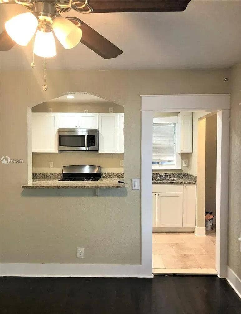 Kitchen featuring white cabinetry, stone-finish countertops, stainless steel microwave, and integrated cooktop with a pass-through opening