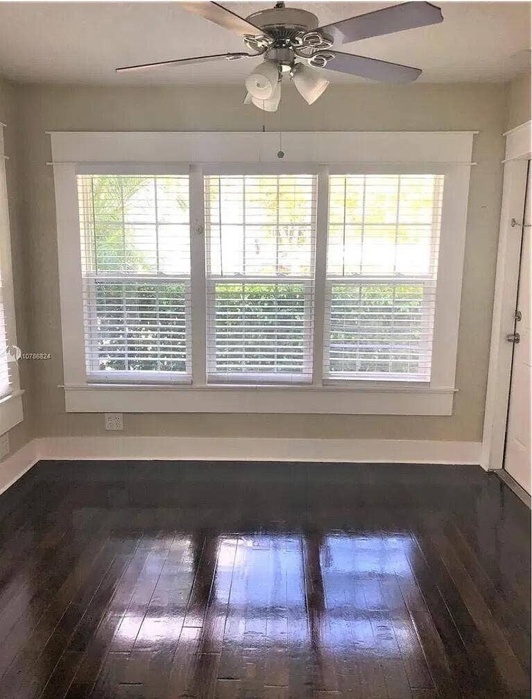 Dark-stained wood-finish flooring, three-panel window configuration with wide casing, and integrated ceiling fan with multi-light fixture