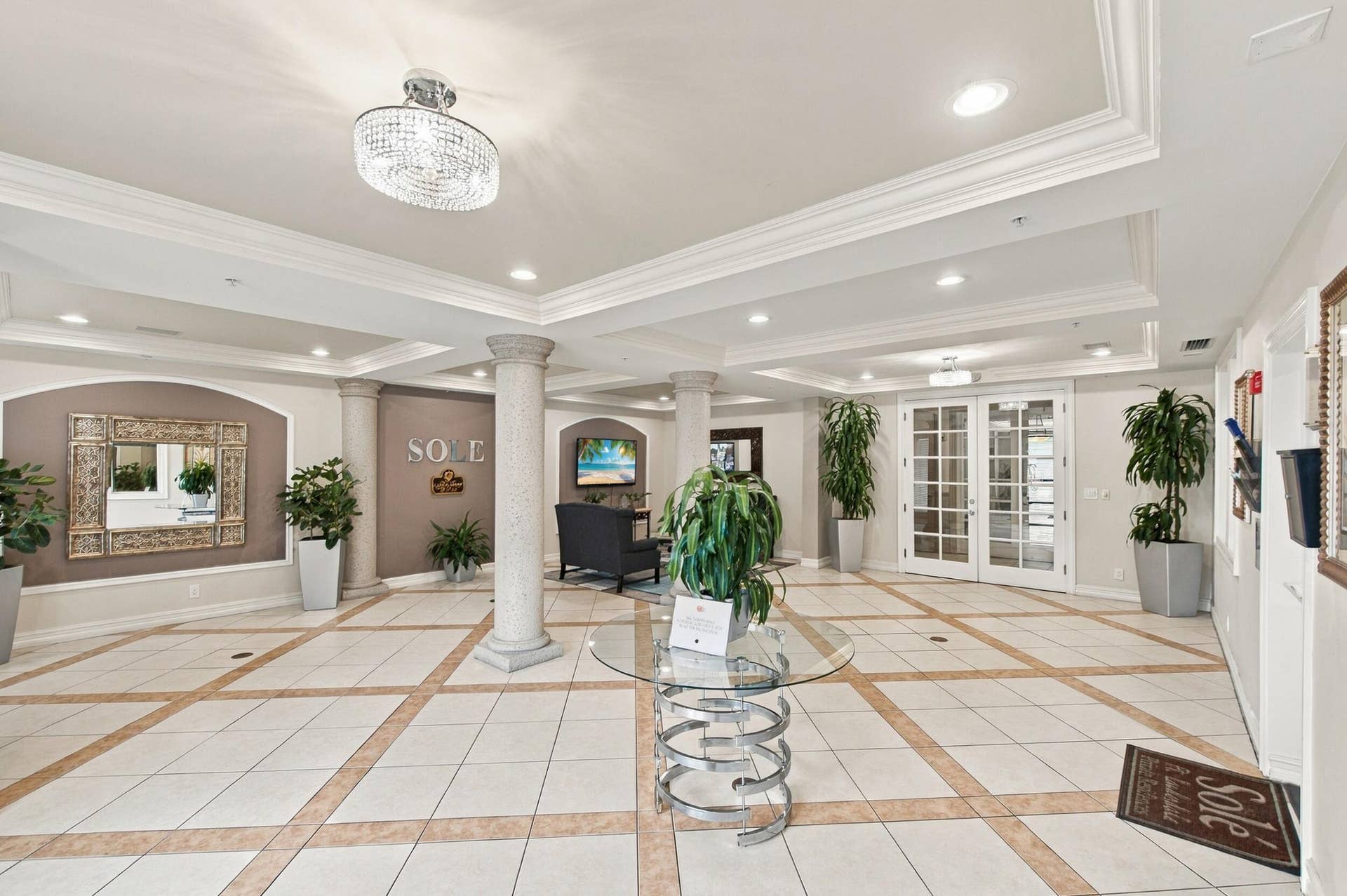 533 NE 3RD Avenue, #202, Fort Lauderdale, FL 33301 Grand lobby entrance featuring tiered tray ceilings, recessed lighting, ornate crystal-style flush mount fixture, classical columns, and decorative tile flooring with inlaid stone-finish borders