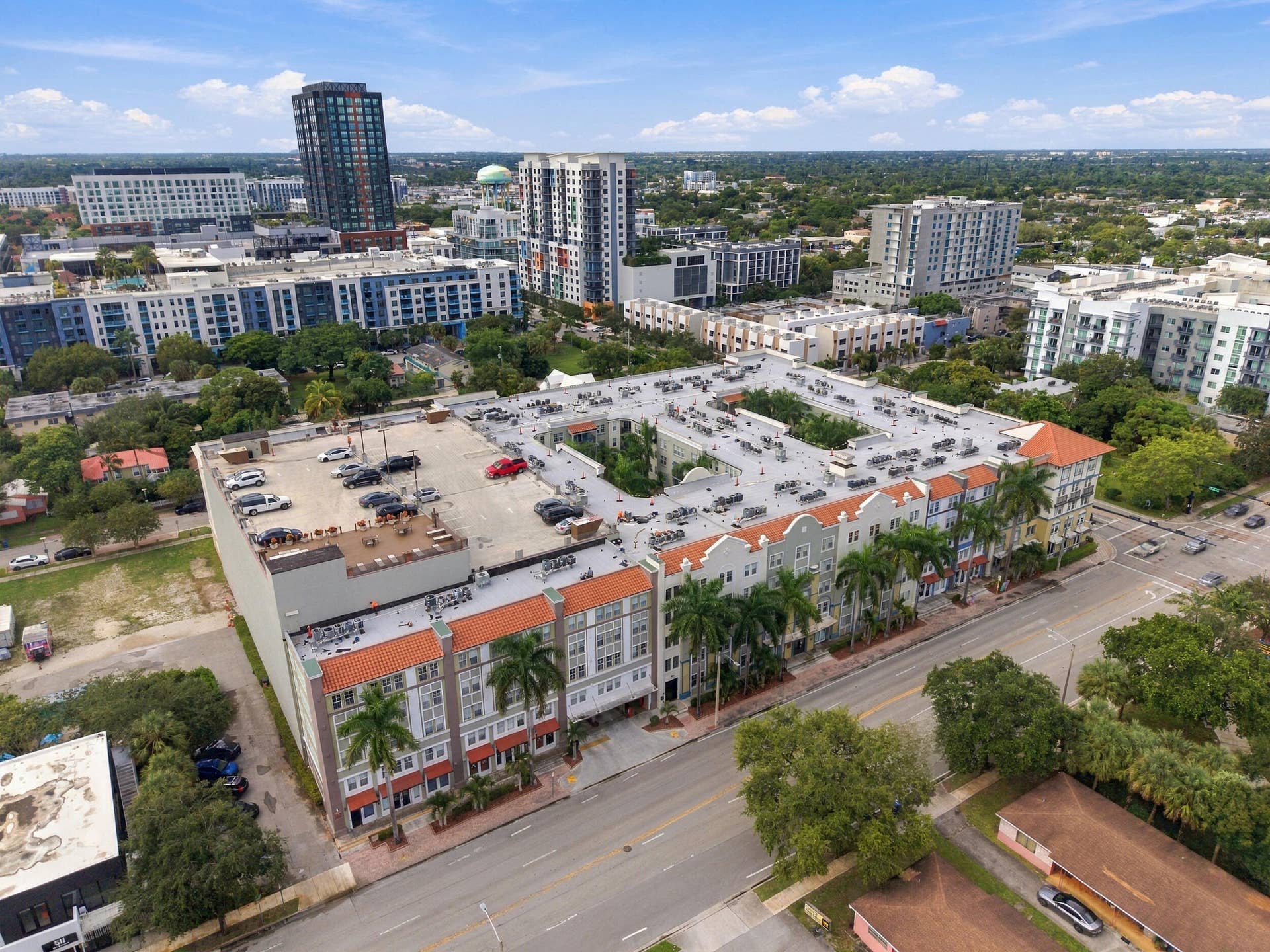 533 NE 3RD Avenue, #202, Fort Lauderdale, FL 33301 Multi-story building with a terracotta-style tiled roof, stucco-finish facade, structured rooftop parking, and exterior palm tree landscaping