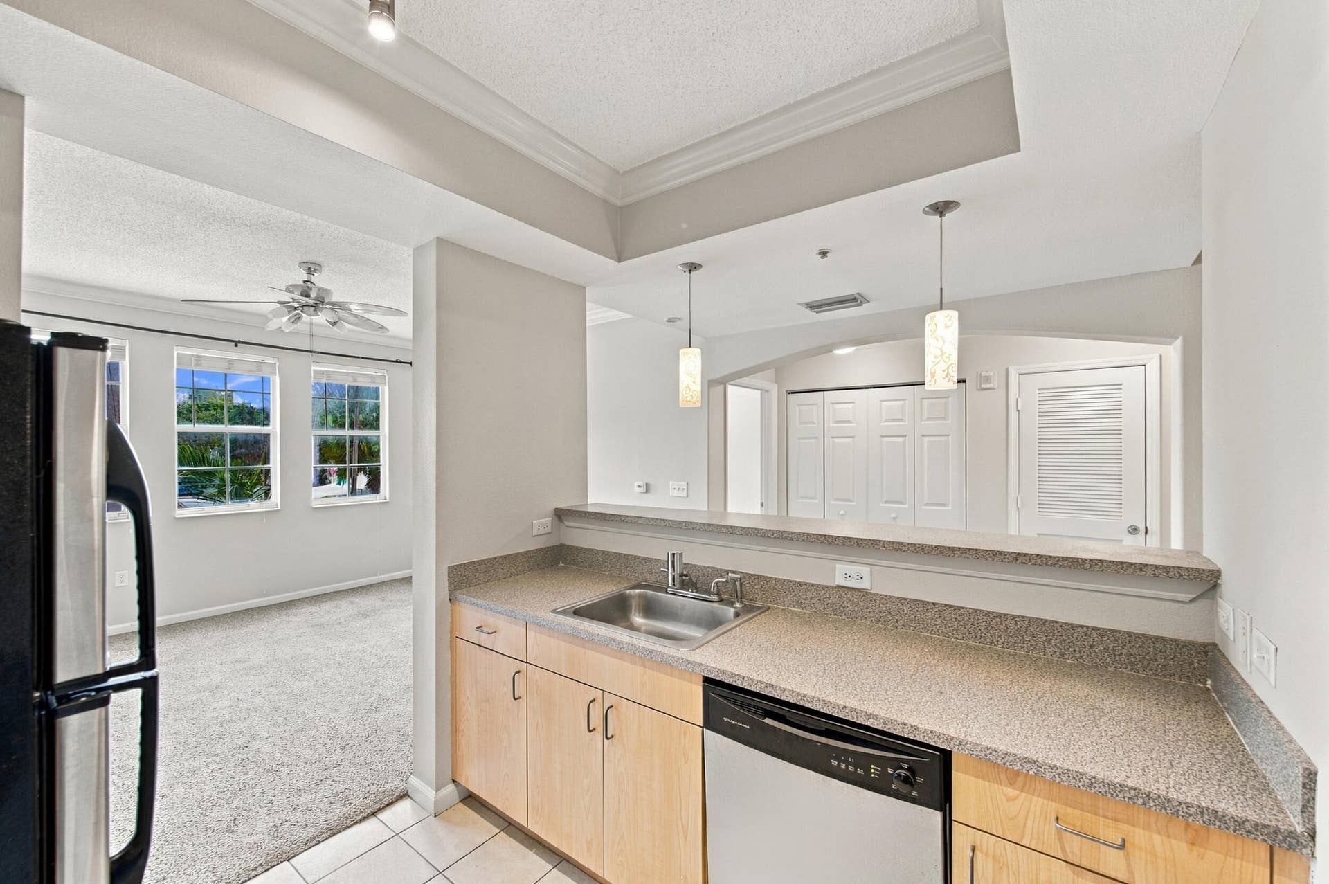 533 NE 3RD Avenue, #202, Fort Lauderdale, FL 33301 Kitchen featuring light wood-tone cabinetry, solid surface countertops, stainless steel undermount sink, and integrated stainless steel dishwasher, illuminated by suspended pendant lighting