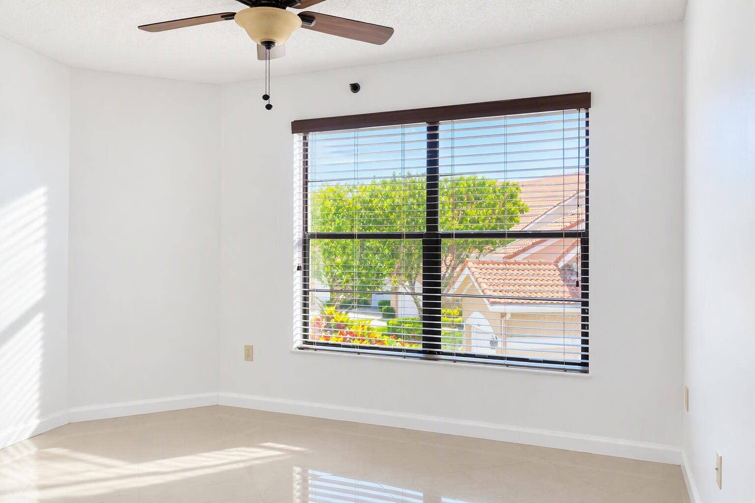 Neutral interior space featuring polished tile flooring, a multi-pane window with dark-frame blinds, and a ceiling fan with integrated lighting