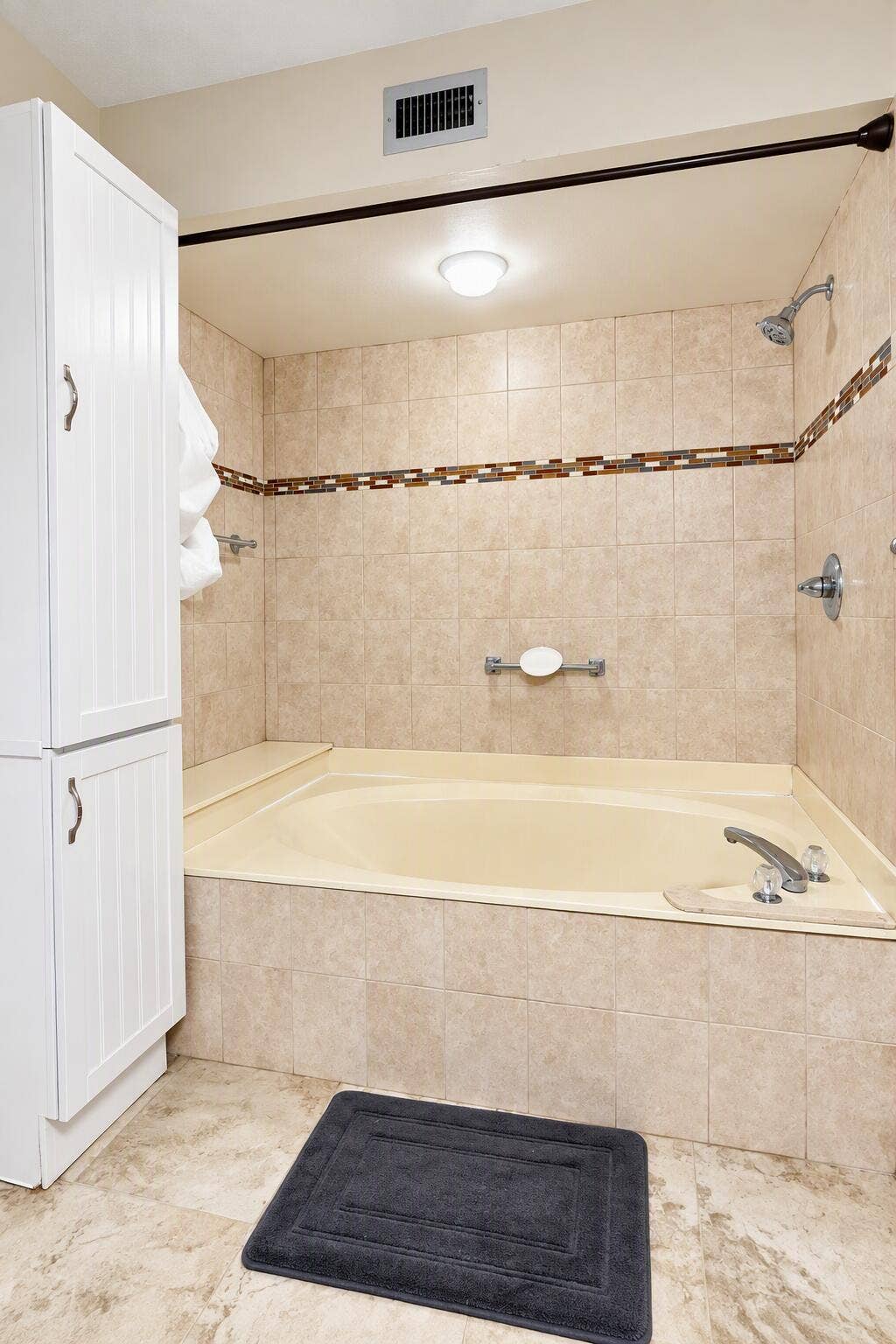 Built-in floor-to-ceiling cabinetry, recessed soaking tub with tiled surround, and decorative tile inlay