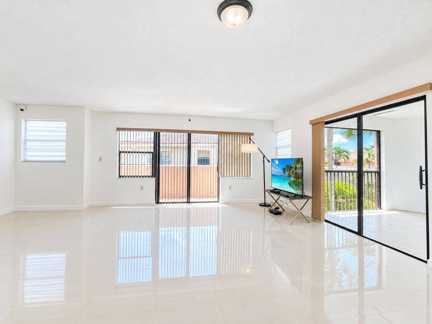 Polished light-toned tile flooring, floor-to-ceiling sliding glass doors, horizontal window blinds, and a flush-mount ceiling light fixture