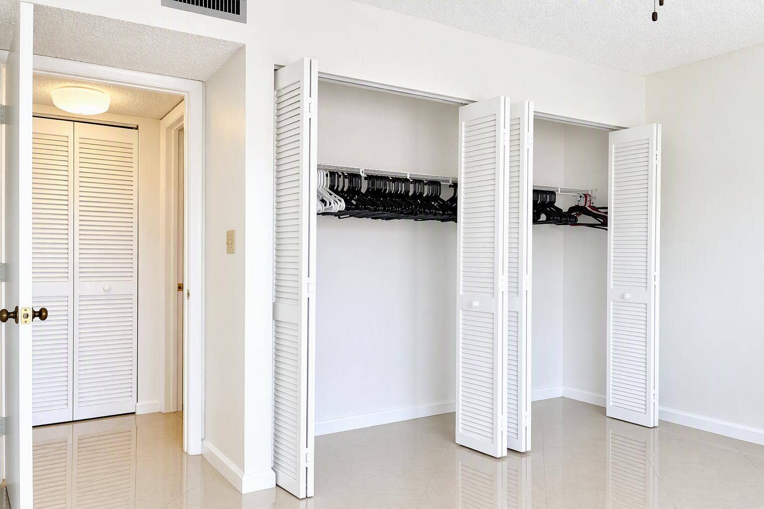 Double closets featuring white bi-fold louvered doors, interior shelving, and smooth-finish flooring