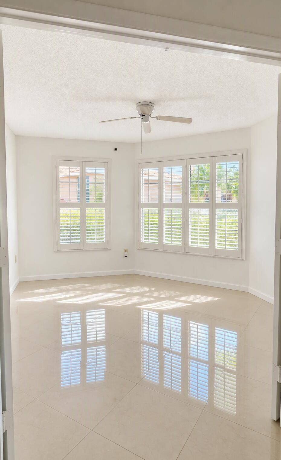 Interior space featuring large-format tile flooring, plantation shutters, and a ceiling fan