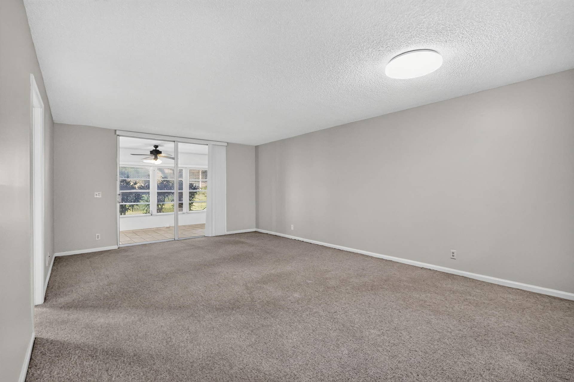 14527 BONAIRE Boulevard, #109, Delray Beach, FL 33446 Neutral-toned interior space featuring wall-to-wall carpeting, a flush-mount ceiling light fixture, and a sliding glass door providing external access