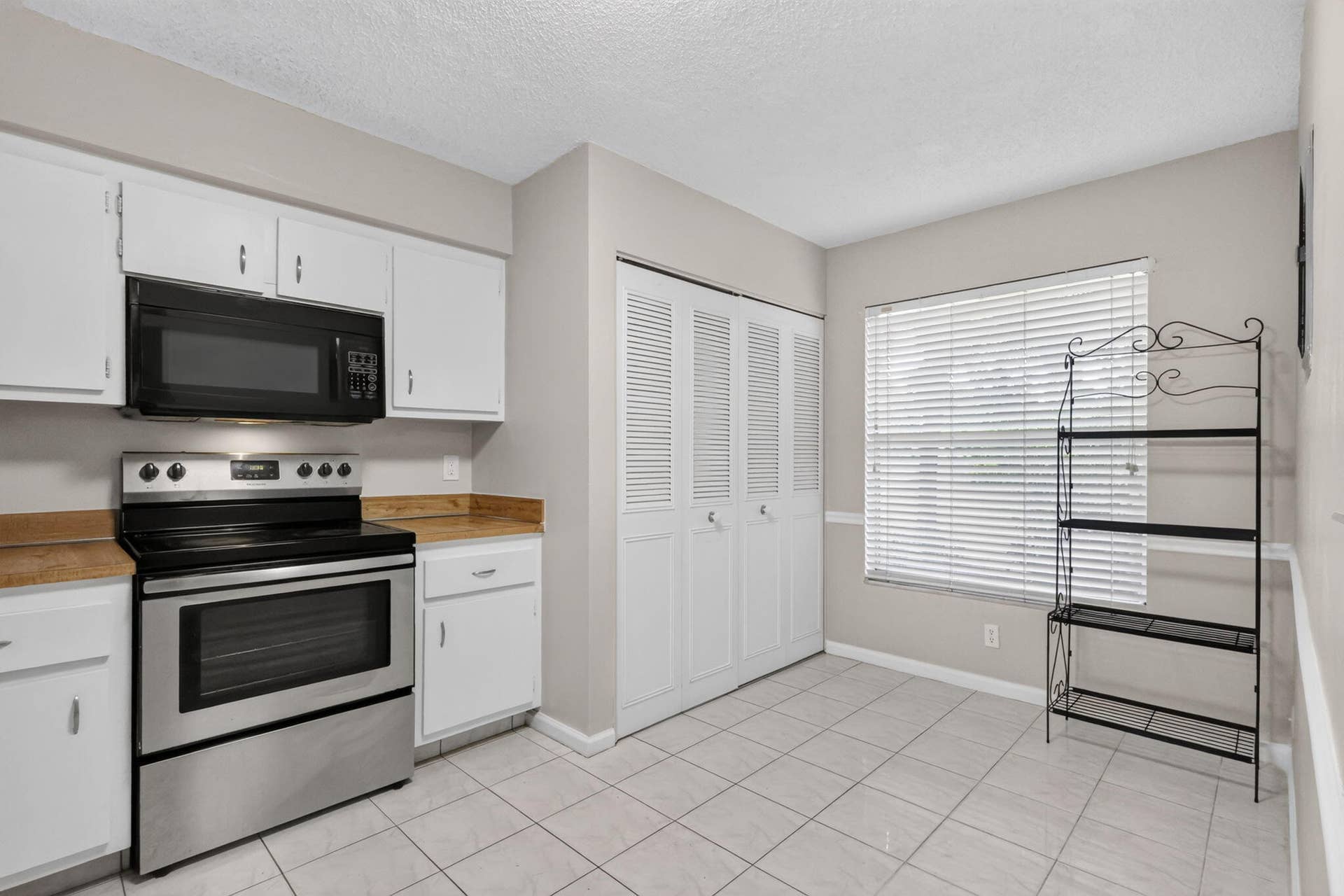 14527 BONAIRE Boulevard, #109, Delray Beach, FL 33446 Kitchen area featuring white cabinetry, stainless steel range with overhead microwave, wood-finish countertops, tile flooring, and louvered closet doors