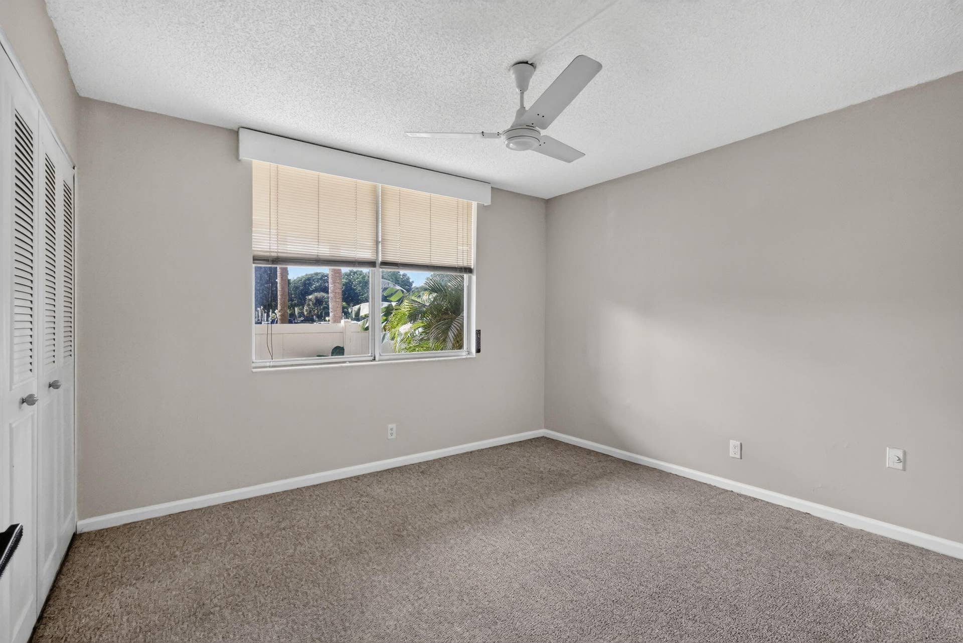 14527 BONAIRE Boulevard, #109, Delray Beach, FL 33446 Room featuring neutral wall tones, wall-to-wall carpeting, white bi-fold closet doors, a white ceiling fan, and a window with a valance