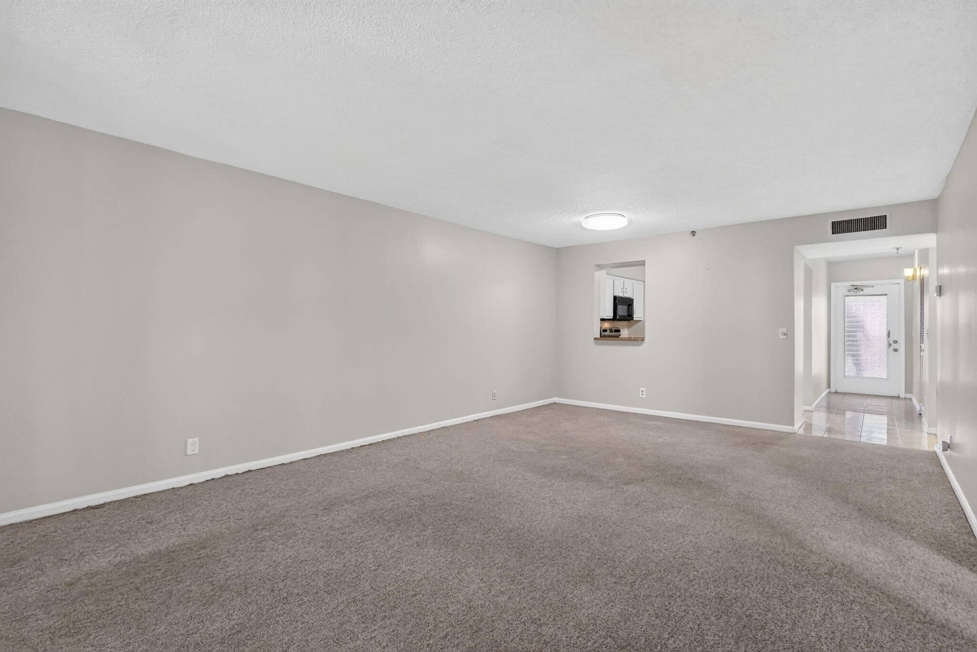 14527 BONAIRE Boulevard, #109, Delray Beach, FL 33446 Neutral wall paint, carpeting, ceiling-mounted lighting, and an interior pass-through opening