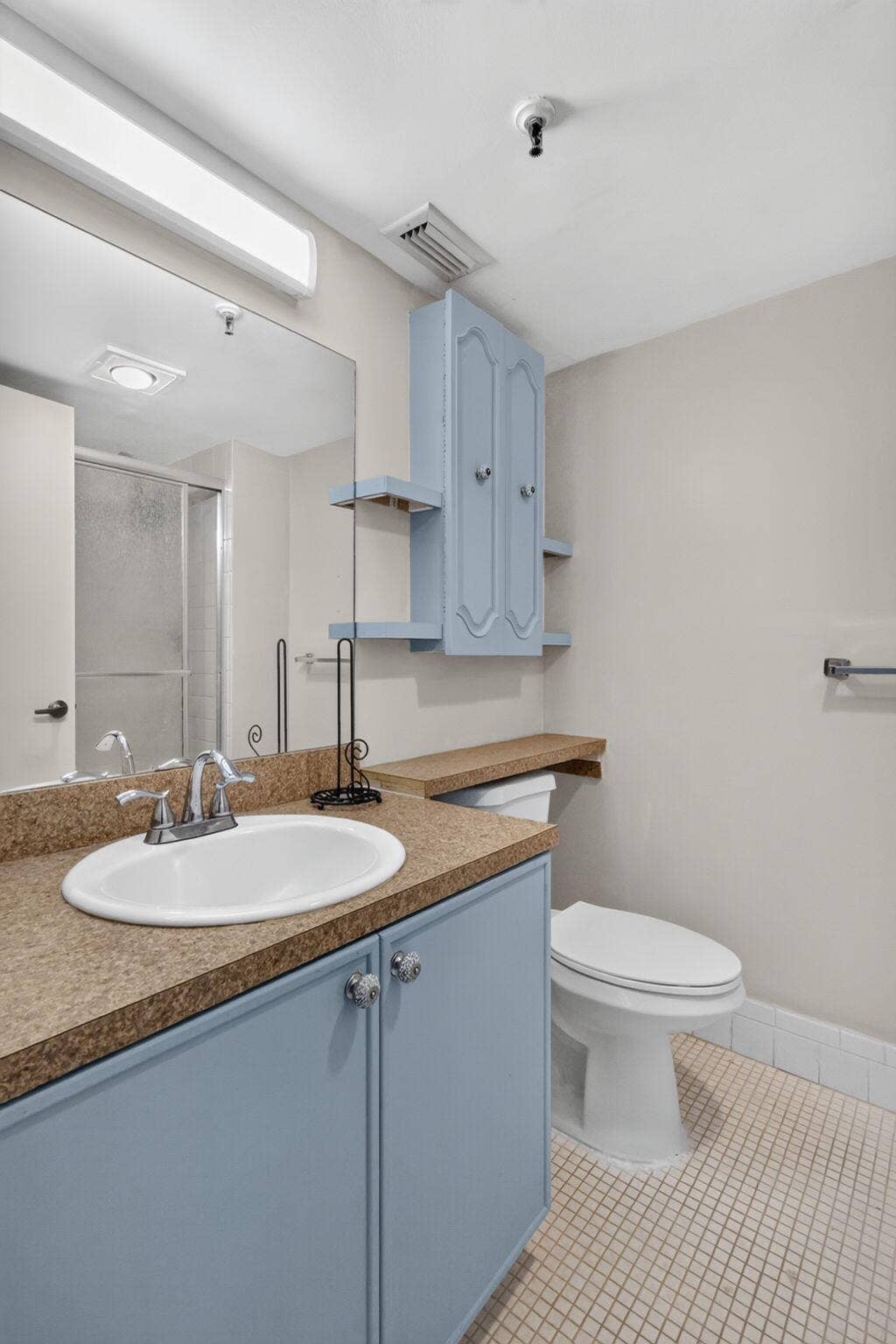 14527 BONAIRE Boulevard, #109, Delray Beach, FL 33446 Bathroom featuring a vanity with light blue cabinetry, a neutral solid-surface countertop, an integrated porcelain sink, wall-mounted storage cabinetry, and a large plate-glass mirror