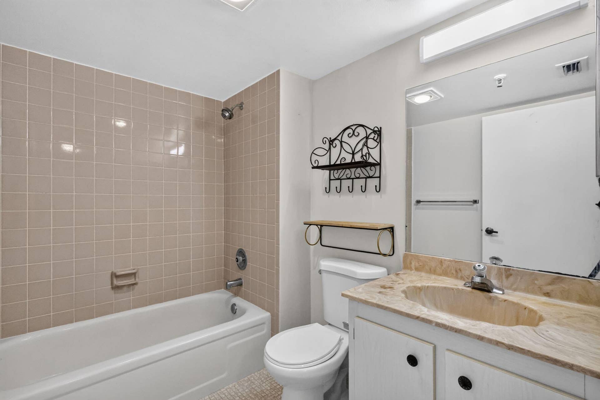 14527 BONAIRE Boulevard, #109, Delray Beach, FL 33446 Bathroom featuring a full-sized bathtub with tile surround, stone-composite vanity countertop with an integrated basin, large wall-mounted mirror, and overhead strip lighting