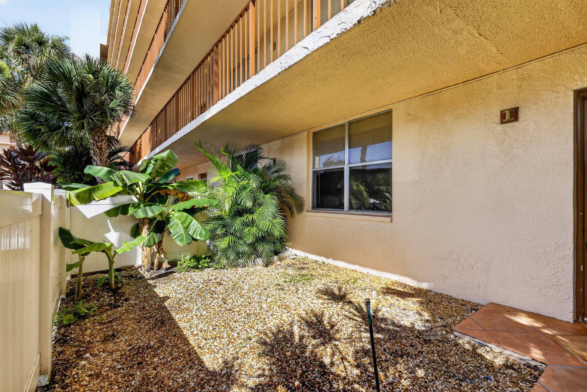 14527 BONAIRE Boulevard, #109, Delray Beach, FL 33446 Stucco exterior featuring an elevated balcony with vertical balustrade, paved entrance area, and low-maintenance rock garden