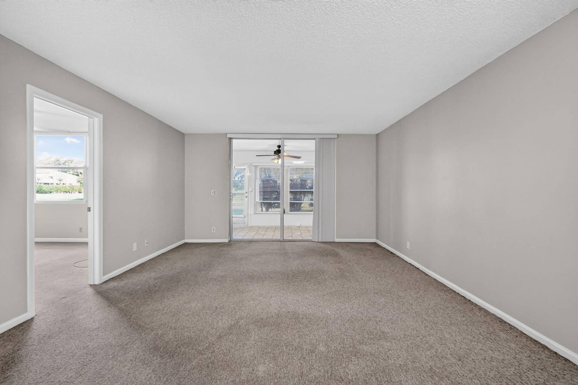 14527 BONAIRE Boulevard, #109, Delray Beach, FL 33446 Spacious interior featuring neutral wall tones, carpeted flooring, and a large sliding glass door with access to the enclosed patio