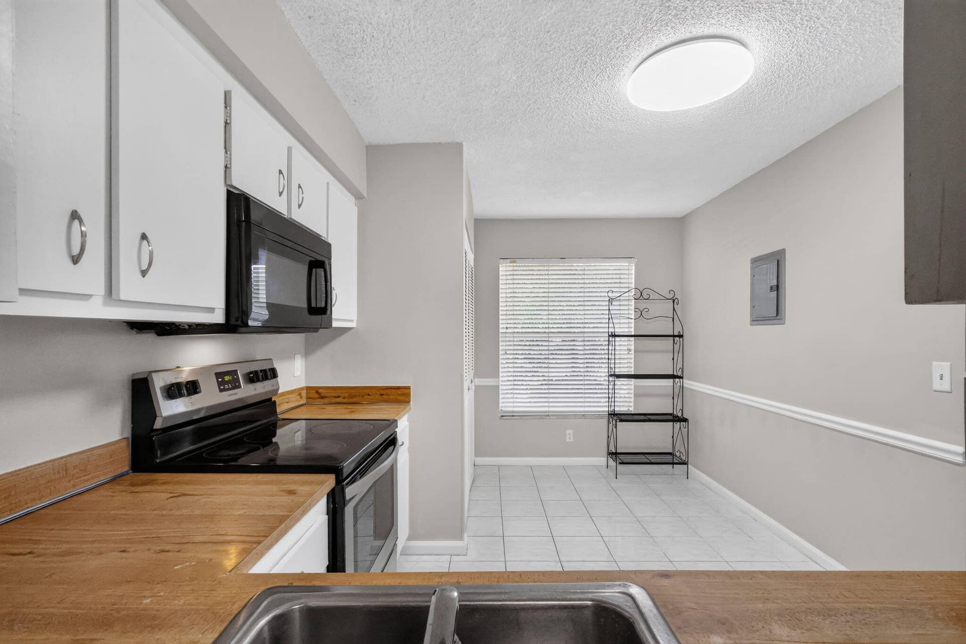 14527 BONAIRE Boulevard, #109, Delray Beach, FL 33446 Kitchen featuring white cabinetry, wood-surface countertops, black integrated appliances, tile flooring, and chair rail molding
