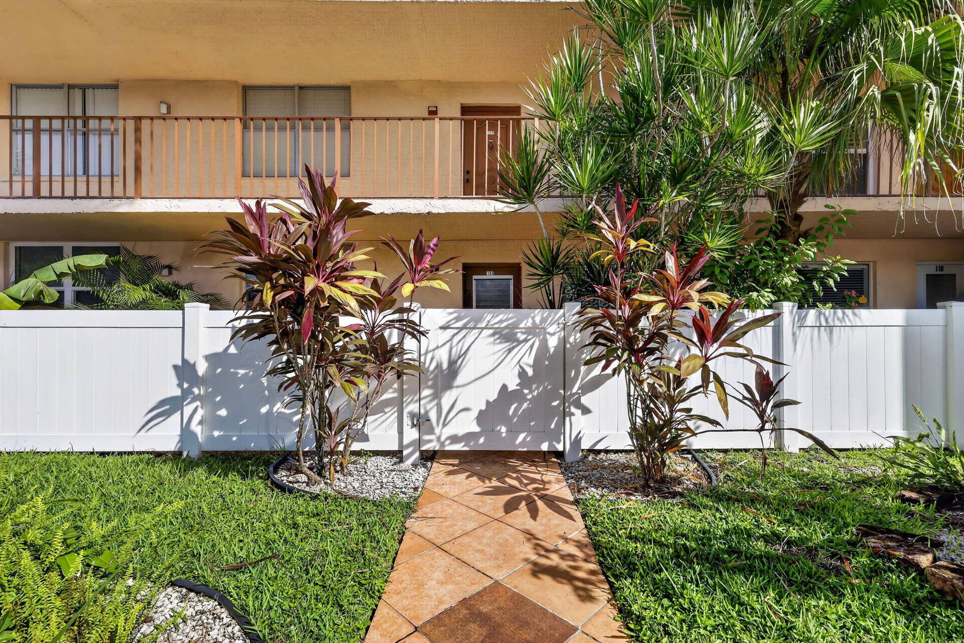 14527 BONAIRE Boulevard, #109, Delray Beach, FL 33446 Private patio featuring a white vinyl privacy fence, terracotta-toned paver walkway, and integrated landscaping