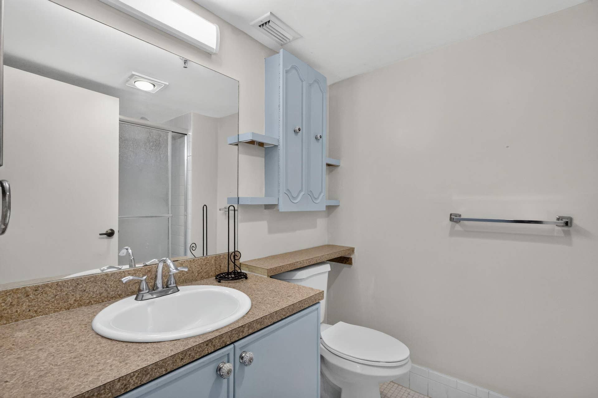 14527 BONAIRE Boulevard, #109, Delray Beach, FL 33446 Bathroom featuring a vanity with a solid-surface countertop, an integrated oval sink, wall-mounted cabinetry with side shelving, a full-width mirror, and a glass-enclosed shower