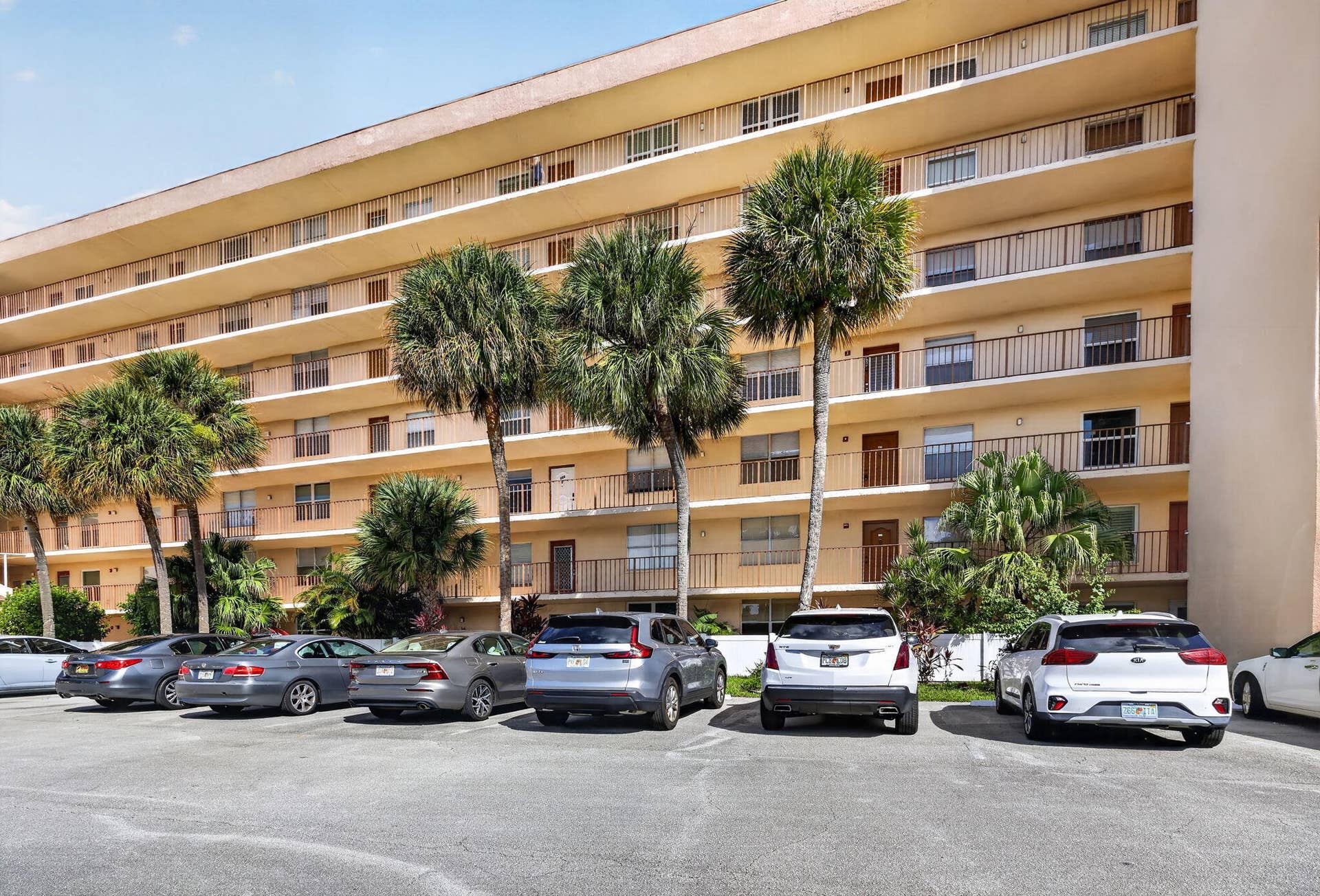 14527 BONAIRE Boulevard, #109, Delray Beach, FL 33446 Multi-story building exterior featuring a curved facade, private balconies with metal railings, and mature palm tree landscaping