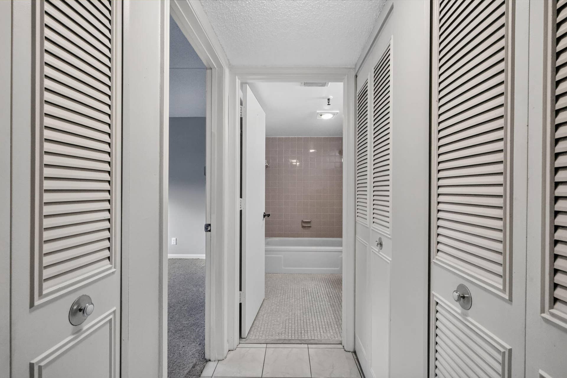 14527 BONAIRE Boulevard, #109, Delray Beach, FL 33446 Hallway featuring dual floor-to-ceiling closets with white louvered doors, tile flooring, and a bathroom containing a tiled shower surround
