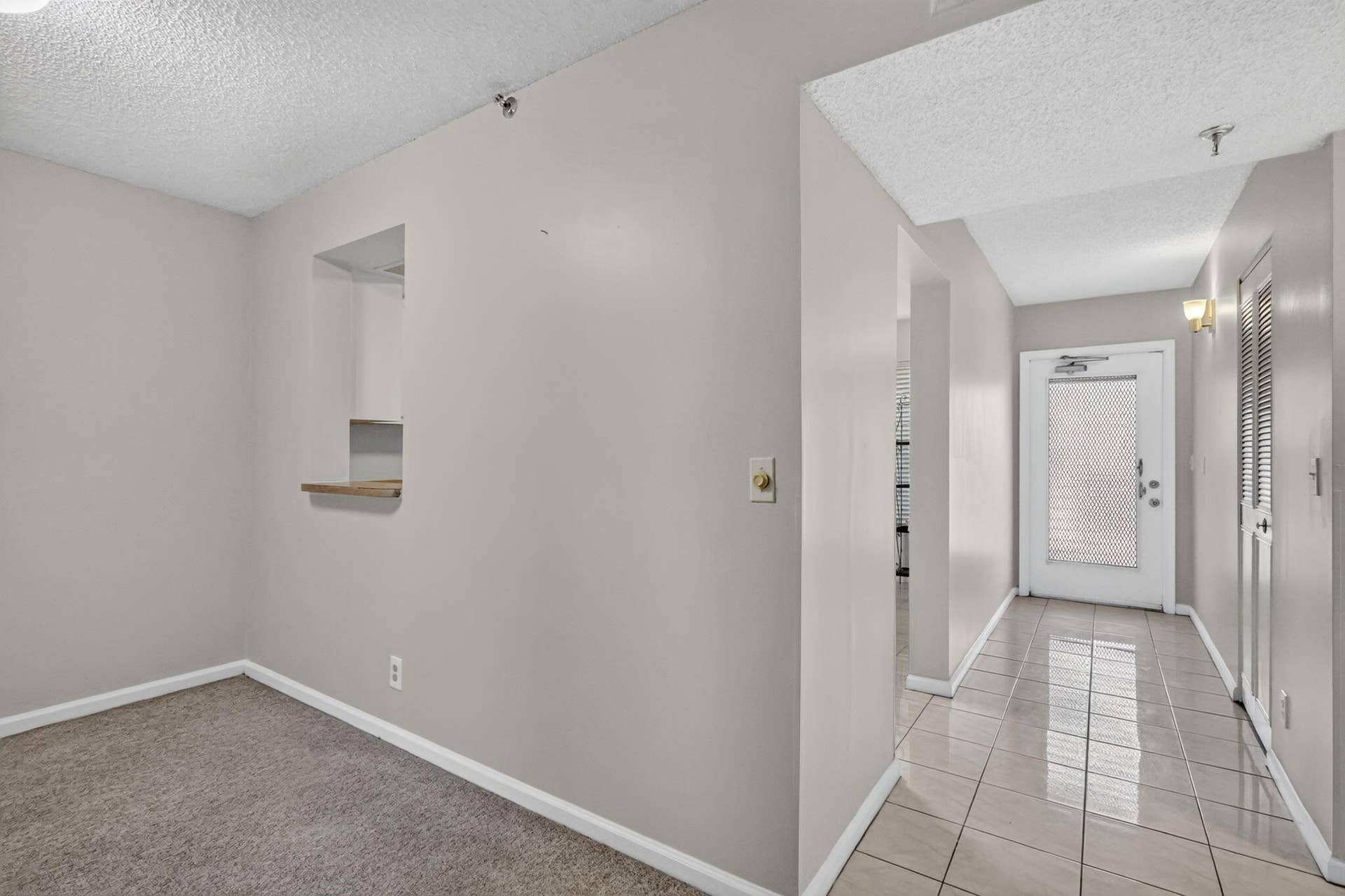 14527 BONAIRE Boulevard, #109, Delray Beach, FL 33446 Interior hallway featuring ceramic tile flooring, a pass-through window with a wood-finish ledge, neutral wall paint, and a door with an inset textured glass panel