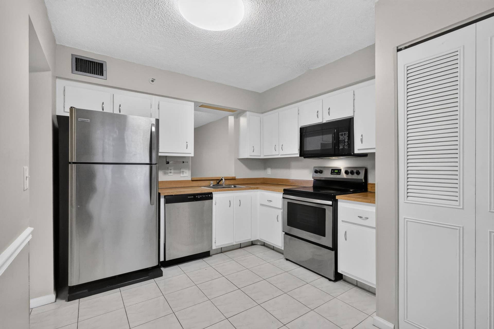 14527 BONAIRE Boulevard, #109, Delray Beach, FL 33446 Kitchen featuring white cabinetry, stainless steel appliances, butcher block countertops, and tiled flooring